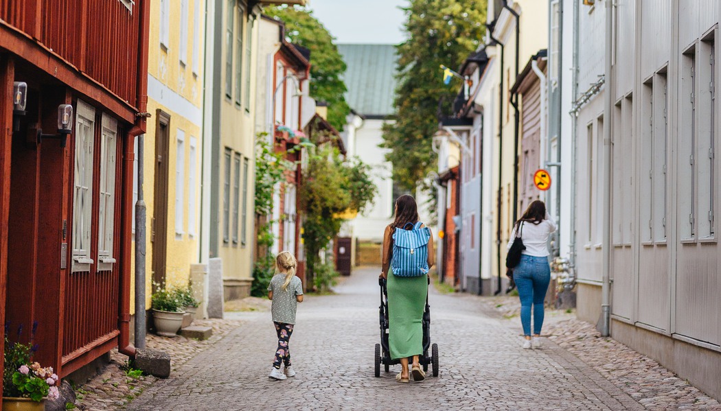 Personer som går på kullerstensgata bredvid gamla trähus.
